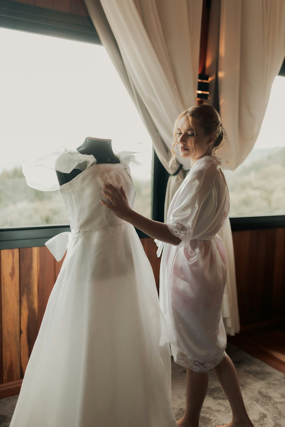 Bride in a robe beside a window before her ceremony